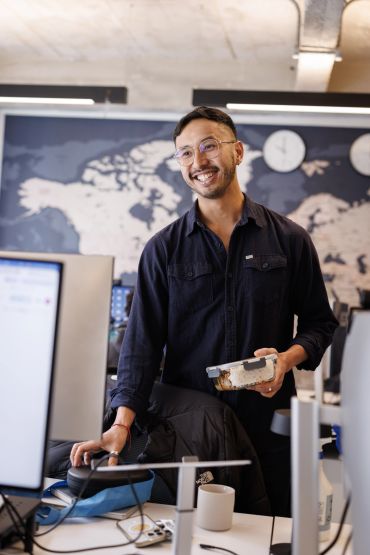 Smiling man holding a lunchbox in an office setting.
