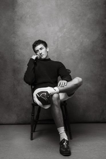 Young man sitting on chair in thoughtful pose.