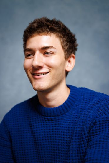 Young man in blue sweater smiling.