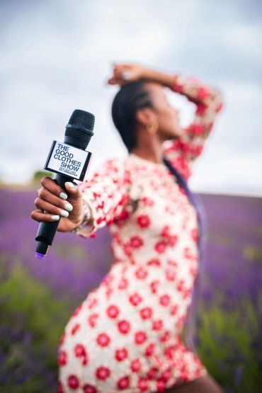 Woman holding a microphone with 'The Good Clothes Show' label outdoors.
