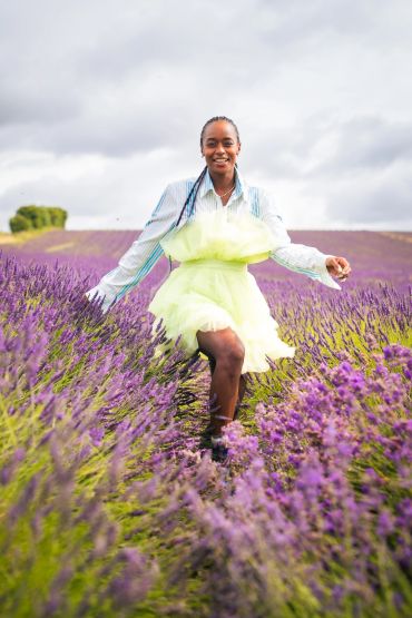 Woman joyfully walking through a vibrant lavender field under a cloudy sky.