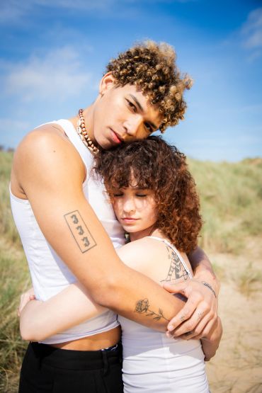 A young couple embracing outdoors under a blue sky.