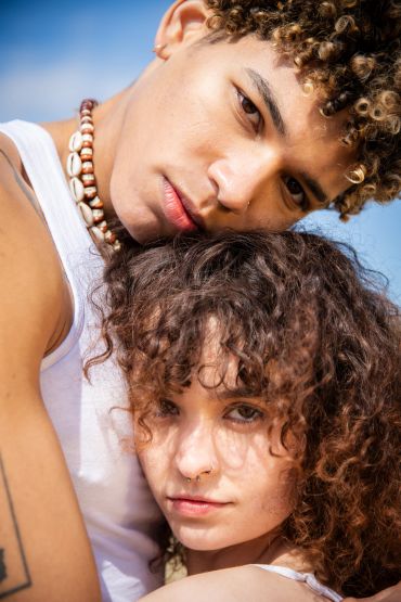 Two young people with curly hair embracing under a clear blue sky.
