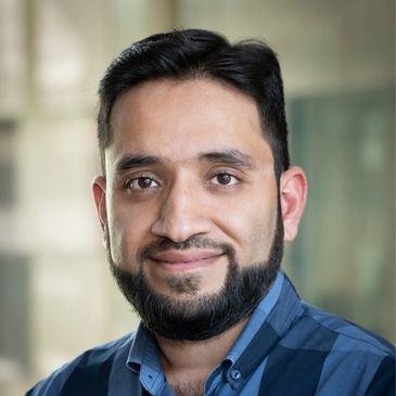 Portrait of a smiling man with a beard and blue checkered shirt.