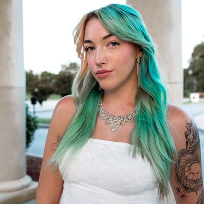 Woman with green hair and tattoos wearing white dress.