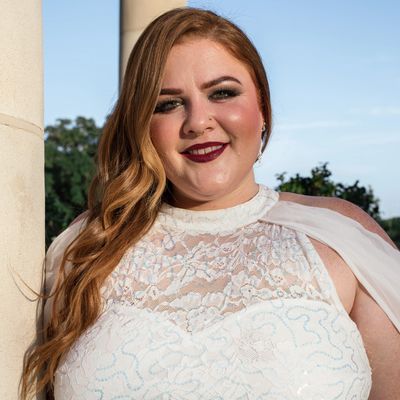 Smiling woman in a white lace dress outdoors.
