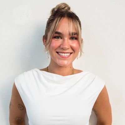 Smiling woman in white top with tattoos and jewelry.