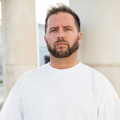 Serious man with a beard and white shirt standing outdoors.