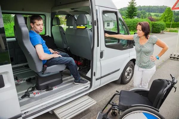 A person sits in a modified van, looking at a woman standing next to a wheelchair outside