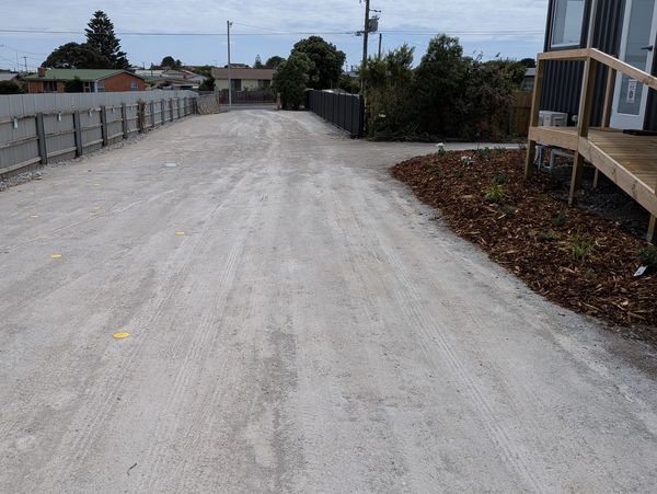 A wide, unpaved road with fences and plants alongside.
