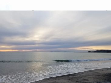 Calm ocean beach under a cloudy sky at sunset.