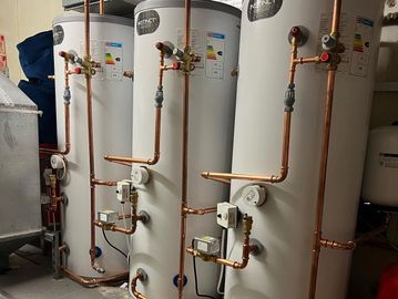 Three large water heaters connected with copper piping in a utility room.