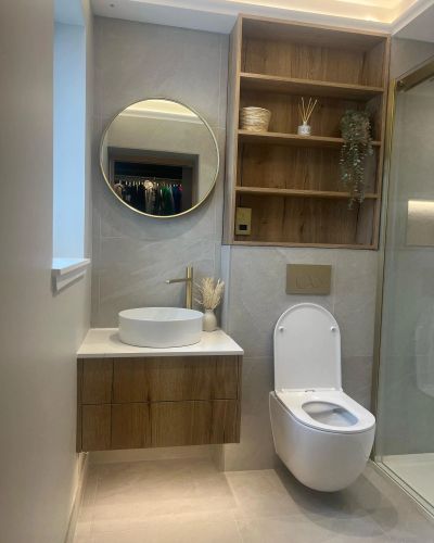 Modern bathroom with round mirror, wooden shelves, and white fixtures.
