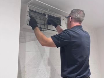 Technician cleaning or repairing a wall-mounted air conditioner unit.