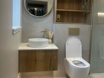 Modern bathroom with wooden vanity, round mirror, and white toilet.