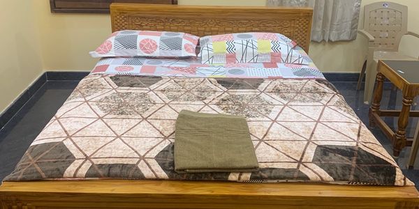 A neatly made wooden bed with patterned sheets and a towel on top in a simple room.