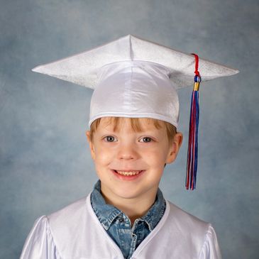 Young graduate in white cap and gown smiling.