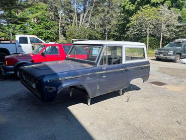 Old blue and white car body shell without wheels in a parking lot.