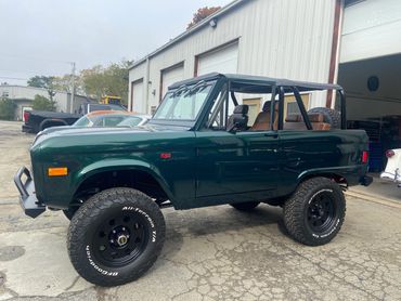 A classic green Ford Bronco with off-road tires parked outside a garage.