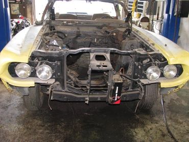 Yellow car with its engine removed in a garage.