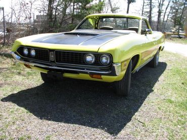A bright yellow vintage muscle car parked outdoors on a sunny day.