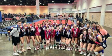 A volleyball team posing with medals in a large indoor venue.