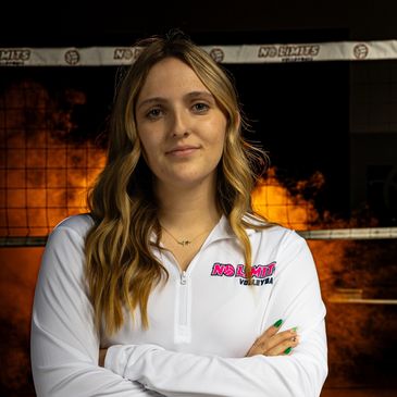 Young woman standing confidently with arms crossed in front of volleyball net with fire backdrop.