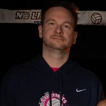 Man in a dark hoodie posing indoors.