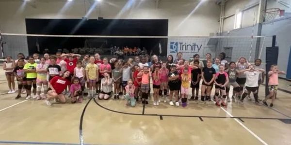 Large group of children posing on an indoor volleyball court.