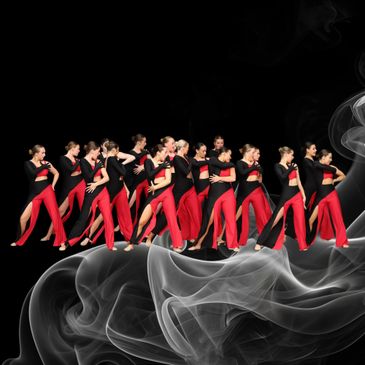 Group of dancers in red and black outfits performing against a smoky black background.