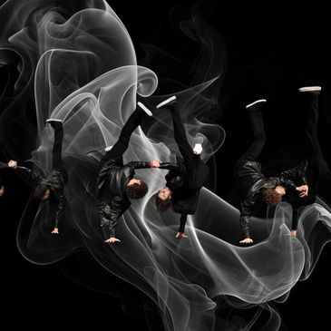 A dancer performs a dynamic flip surrounded by swirling smoke effects.