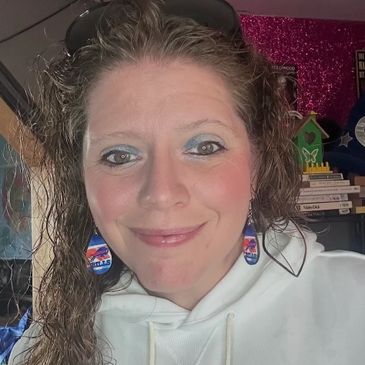 Woman with curly hair wearing colorful earrings and a white hoodie.