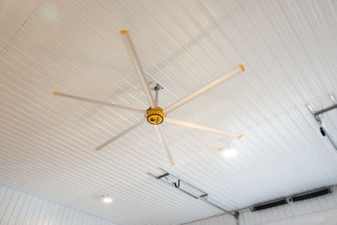 Large ceiling fan with five blades in a white room.