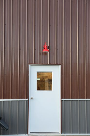 White door on a brown metal wall with a red light above.