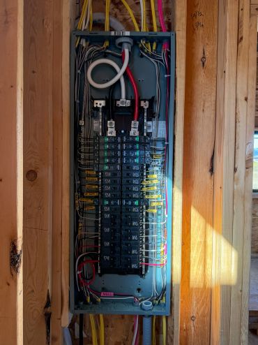 Electrical panel with multiple circuit breakers inside wooden frame.