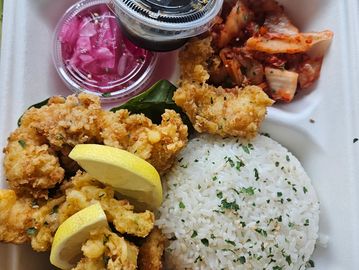 Fried shrimp with rice, lemon, and sides in a takeout container.