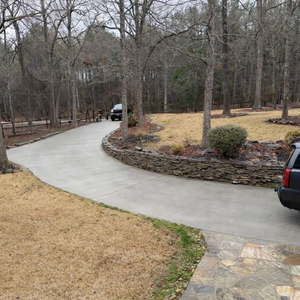 Curved concrete driveway with stone retaining wall and leafless trees.