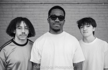 Black and white portrait of three young men against a brick wall.