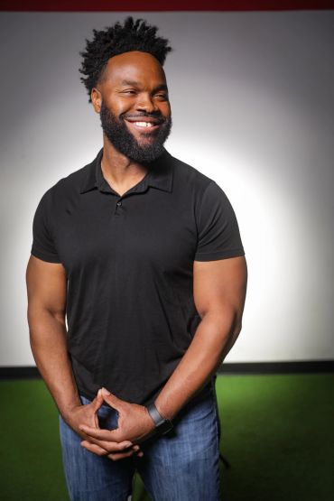Smiling man with a beard and afro hairstyle in casual attire.