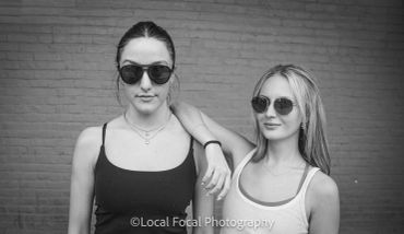 Two women wearing sunglasses posing in front of a brick wall.