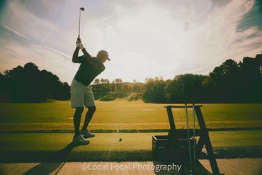 Man swinging golf club toward sunrise.
