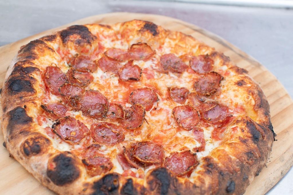 Pepperoni pizza with a slightly charred crust on a wooden board.