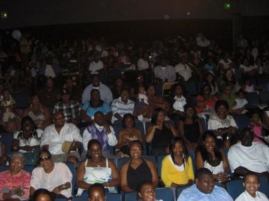 Audience seated in a dimly lit theater or auditorium.