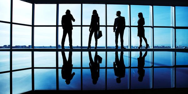 Silhouettes of four business professionals with reflections against large windows.