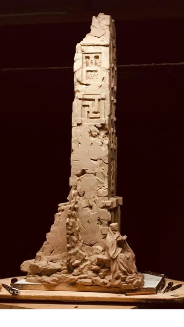 Clay sculpture of a tall ancient pillar with a seated figure at the base.