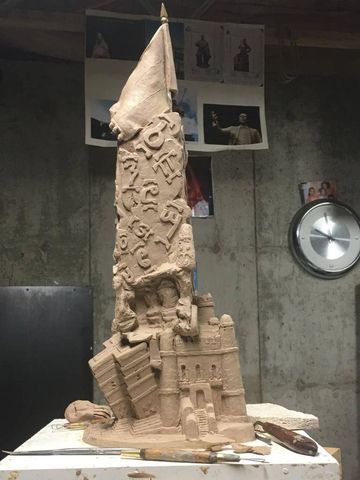 Intricate clay sculpture of a tall monument with symbols and a castle base.