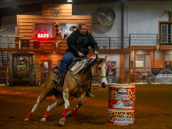 Woman riding a horse around a barrel indoors during a rodeo event.