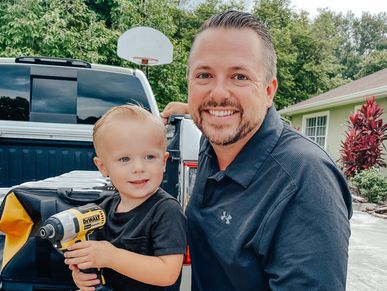 Andy smiling with his son holding a power tool ready for the construction site
