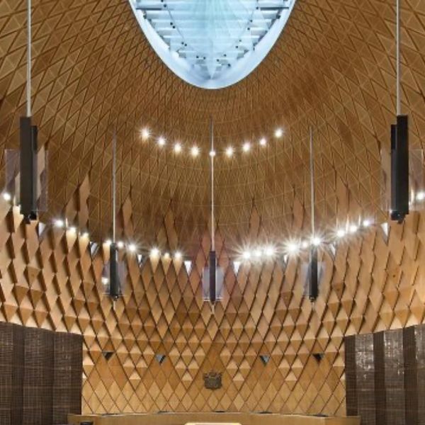 Modern auditorium with geometric wooden ceiling and circular chandelier.
