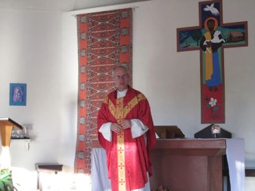 A priest stands in a chapel wearing red liturgical vestments.